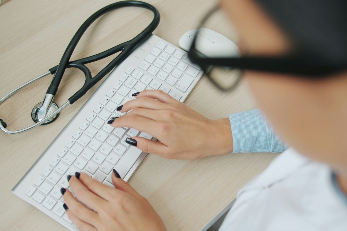 Person typing on keyboard with stethoscope nearby.