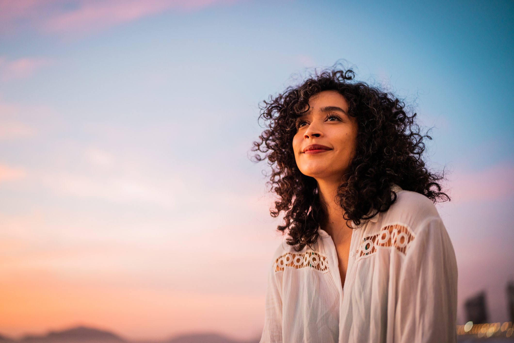Woman smiling at sunset, wearing white blouse.