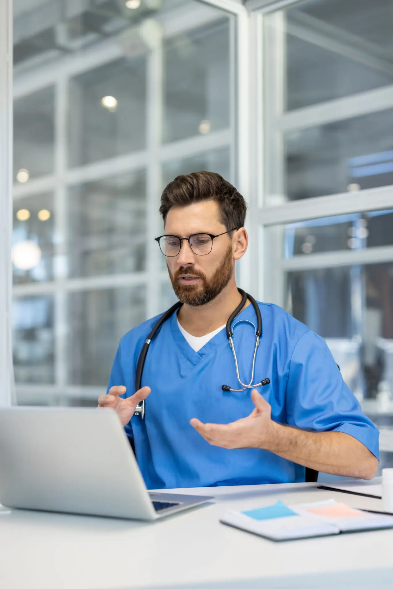 Doctor in blue scrubs using laptop.