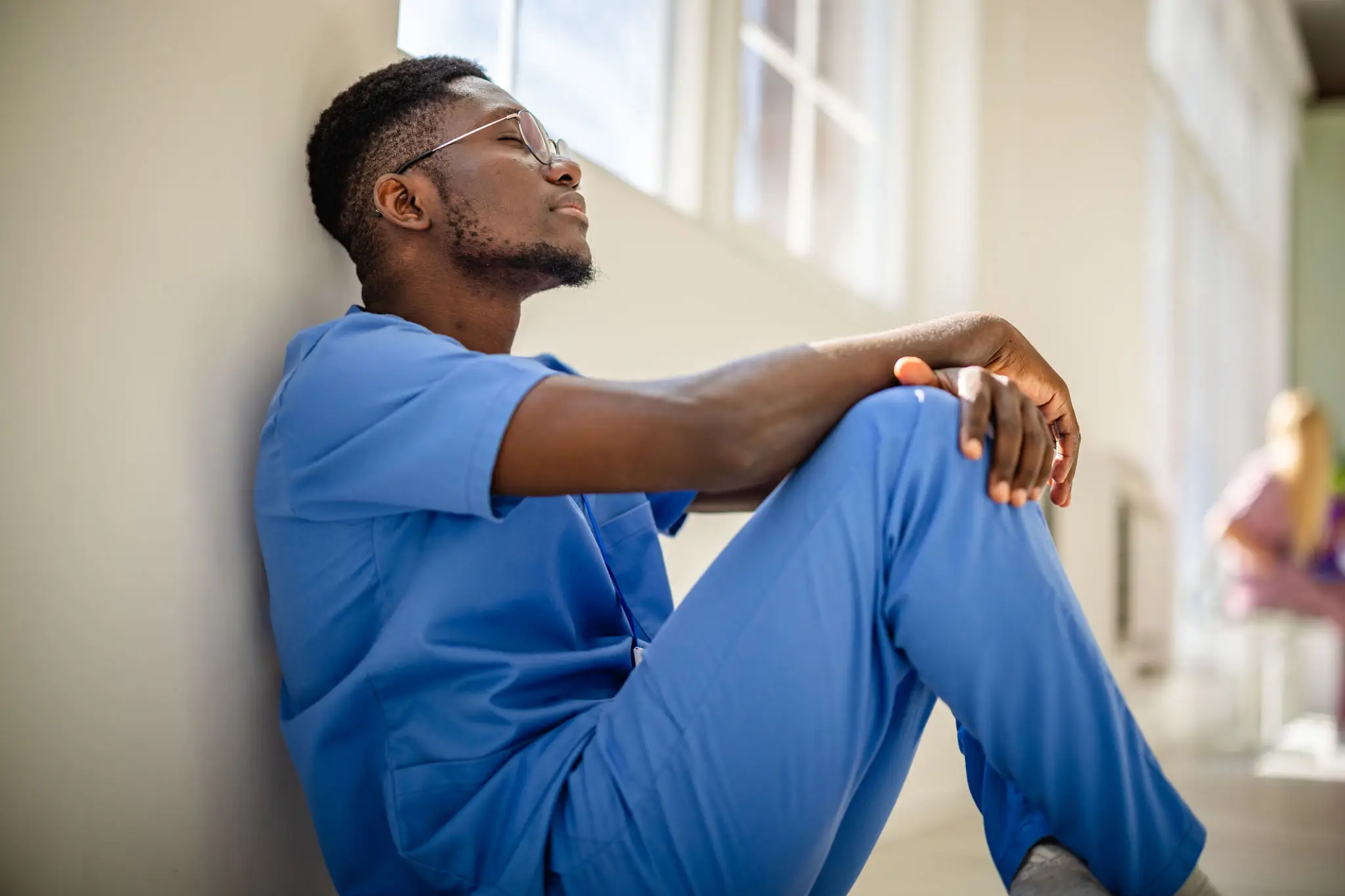 Person in scrubs sitting, looking thoughtful.