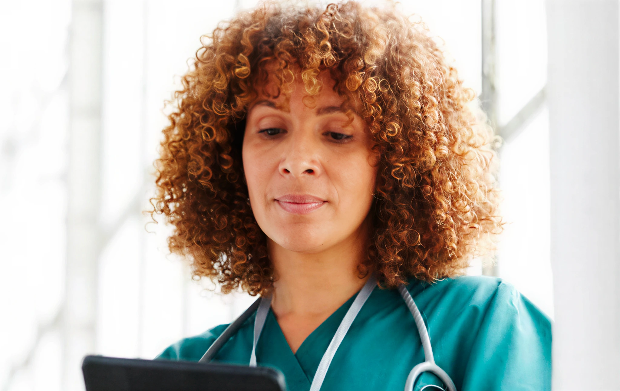 Healthcare professional reading tablet with stethoscope.